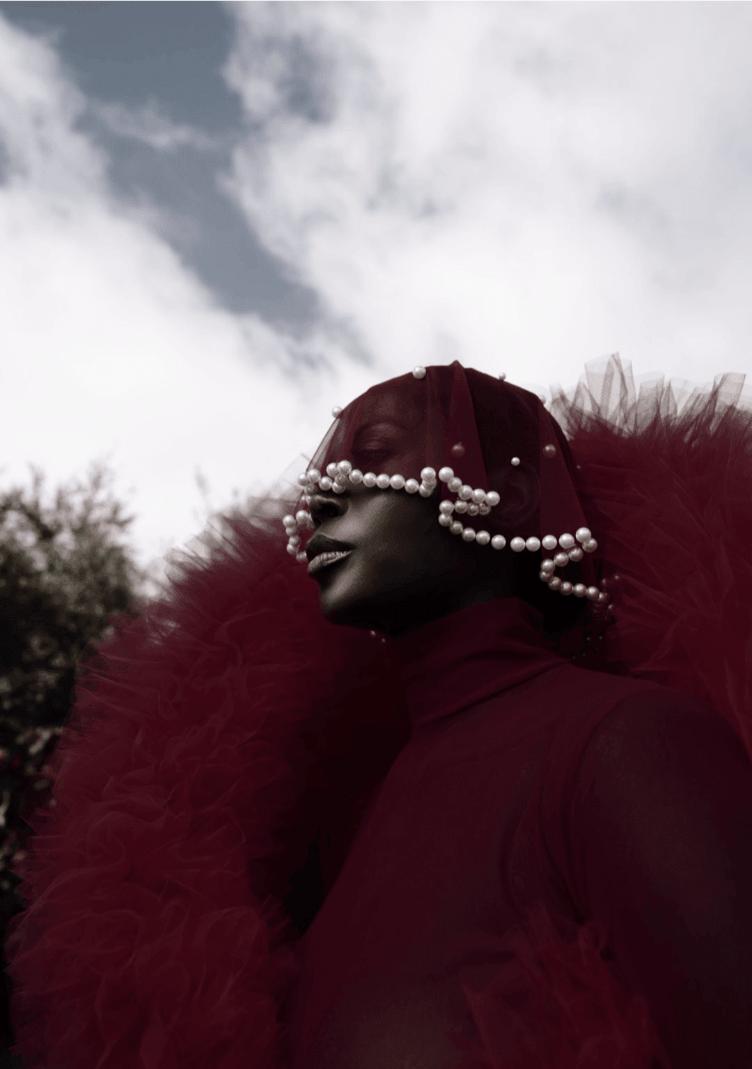A model wearing a striking red tulle outfit with a pearl-embellished veil, reflecting the bold, cultural storytelling approach of fashion stylist and entrepreneur Jenny Ubebe. This image captures Jenny's signature blend of high fashion, personal heritage, and artistic expression in her work.