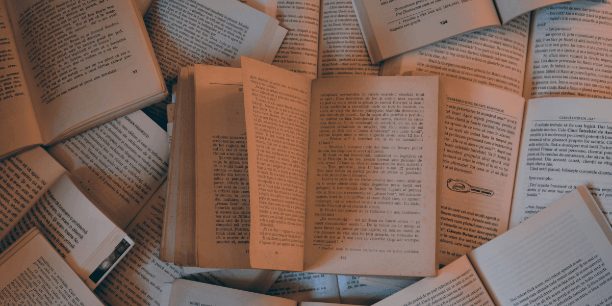 A collection of open books scattered on a surface, displaying pages with text in a warm, soft lighting.