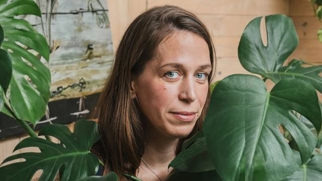 Portrait of artist Laila Seidel surrounded by large green leaves.